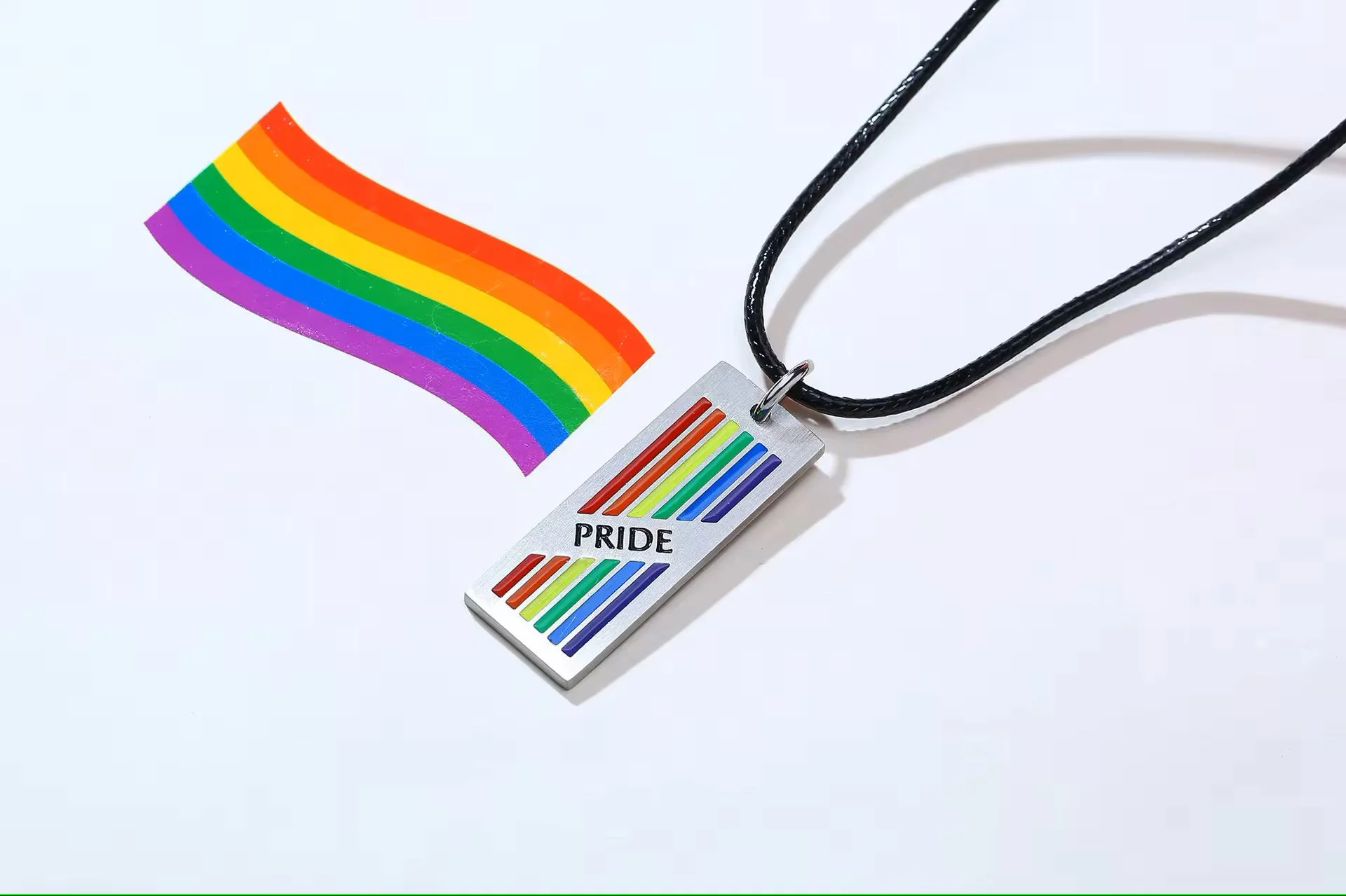  Rainbow Pride Rectangle Pendant with Rope Chain next to a rainbow