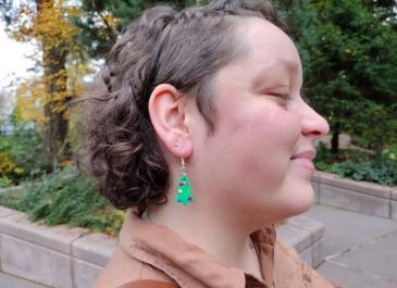 Woman wearing Christmas tree earrings with rainbow colored ornaments